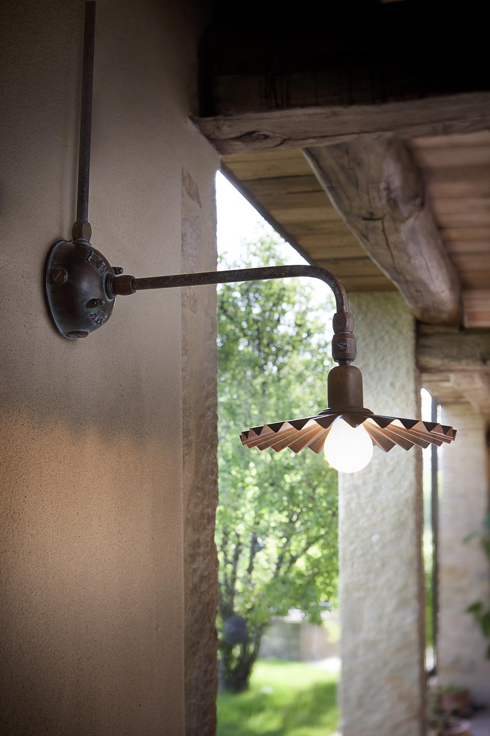 Aged brass wall lamp with rounded arm and pleated reflector. Aldo Bernardi. 